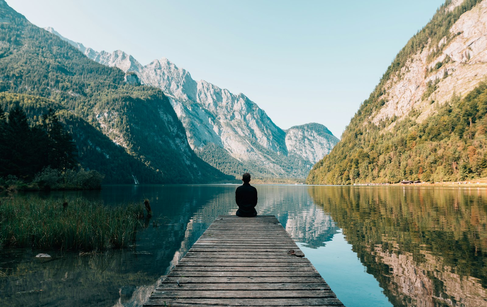 Traveller sitting on a wooden jetty looking across a mountain lake
